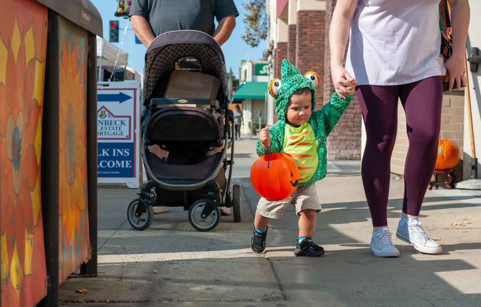 A young boy dressed as a chameleon holds his jack-o-lantern as he makes his way to the 2019 downtown Trick-or-Treat event in Salinas, Calif, on Saturday, Oct. 26, 2019.