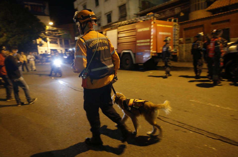 A Civil Protection worker and his search dog patrol a street near the "Tower of David" skyscraper, which suffered an inclination after a powerful earthquake shook eastern Venezuela, causing buildings to be evacuated in the capital of Caracas, Venezuela, Tuesday, Aug. 21, 2018. The quake was felt as far away as Colombia's capital and in the Venezuelan capital office workers evacuated buildings and people fled homes. (AP Photo/Ariana Cubillos)