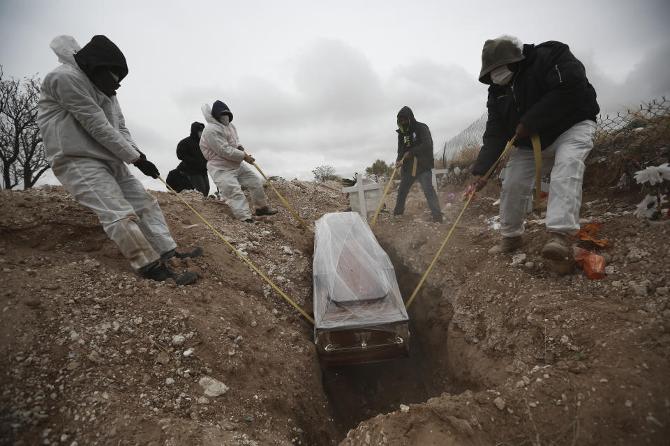 FILE - In this Oct. 27, 2020 file photo, workers wearing full protection gear amid the new coronavirus pandemic, lower a coffin into a grave in an area of the San Rafael municipal cemetery set apart for people who have died from COVID-19, in Ciudad Juarez, Mexico. As Mexico approaches 200,000 in officially test-confirmed deaths from COVID-19, the real death toll is probably higher due to the country’s extremely low rate of testing. (AP Photo/Christian Chavez, File)