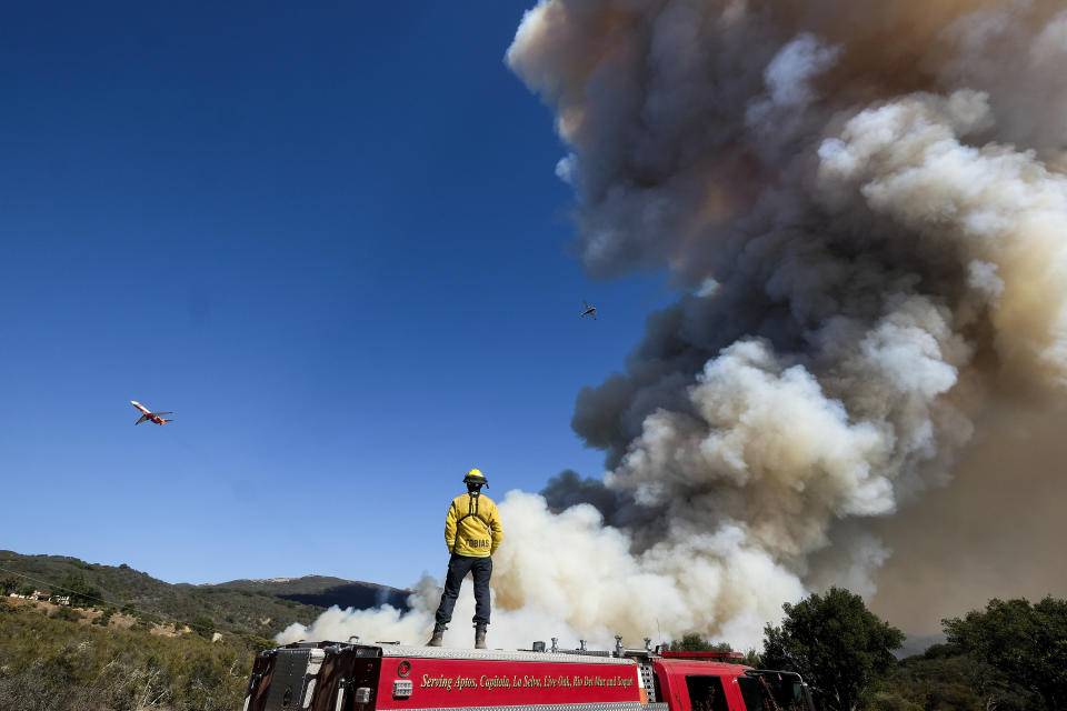 A firefighter watches on his fire engine as smoke rises from a wildfire Wednesday, Oct. 13, 2021, in Goleta, Calif. A wildfire raging through Southern California coastal mountains threatened ranches and rural homes and kept a major highway shut down Wednesday as the fire-scarred state faced a new round of dry winds that raise risk of flames. The Alisal Fire covered more than 22 square miles (57 square kilometers) in the Santa Ynez Mountains west of Santa Barbara. (AP Photo/Ringo H.W. Chiu)