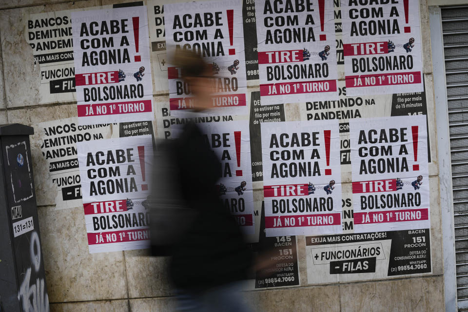 A woman walks past signs that read in Portuguese: "End the Agony, Bolsonaro Out," in Rio de Janeiro, Brazil, Friday, Sept. 30, 2022. Bolsonaro had held forward the possibility of a corruption-free Brazil, but once he took office he was ensnared in his own corruption scandals, including recent claims that members of his family bought dozens of properties in cash. (AP Photo/Matias Delacroix)