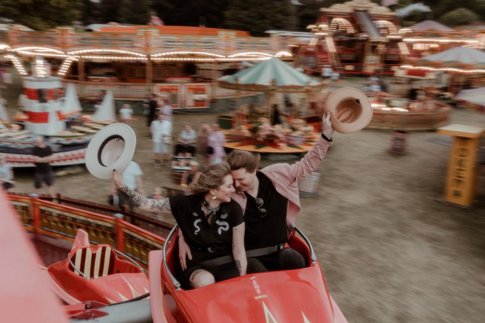 The couple snuggling on an amusement ride and holding up their hats