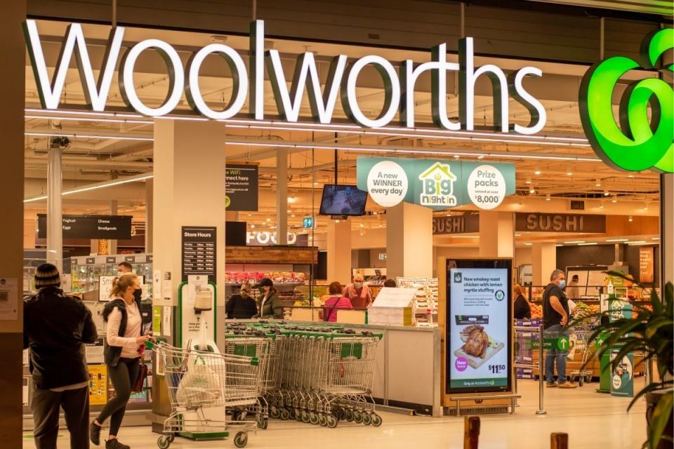 Woolworths shoppers wearing masks wheel trolleys of groceries out of supermarket.