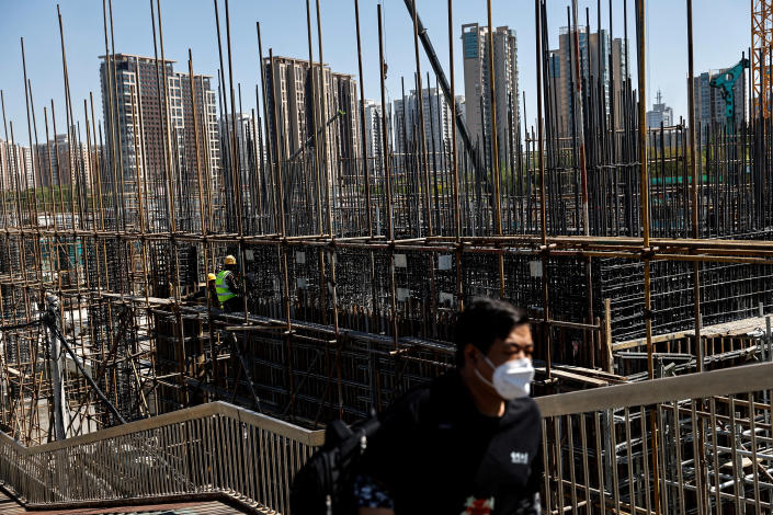 A man walks on an overpass near a construction site with tall buildings in the background.