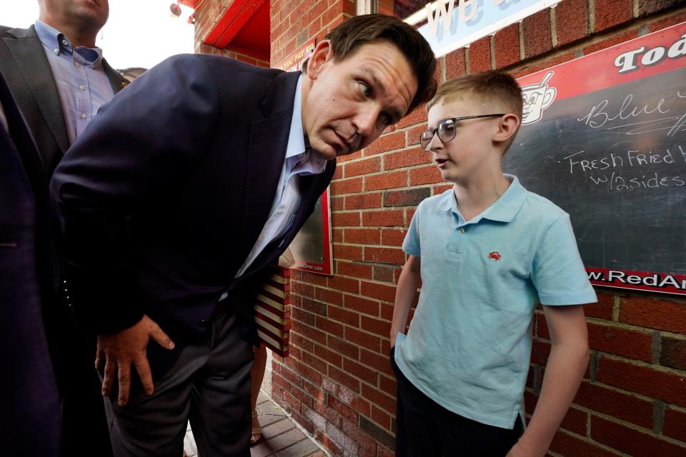 Gov. Ron DeSantis crouches to listen to a child speak.