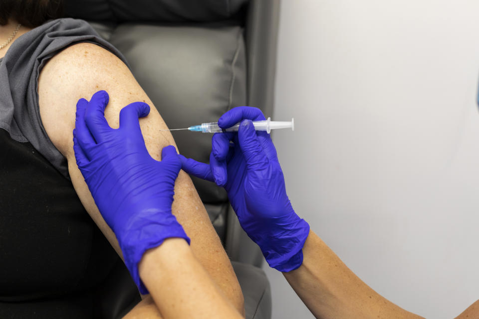 Human hands in protective purple gloves injecting into a persons upper arm.