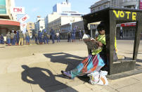 A newspaper vendor reads a copy of a daily paper as police block a main road ahead of a planned protest in Harare, Friday, Aug. 16, 2019. Zimbabwe's police patrolled the streets of the capital Friday morning while many residents stayed home fearing violence from an anti-government demonstration planned by the opposition. (AP Photo/Tsvangirayi Mukwazhi)