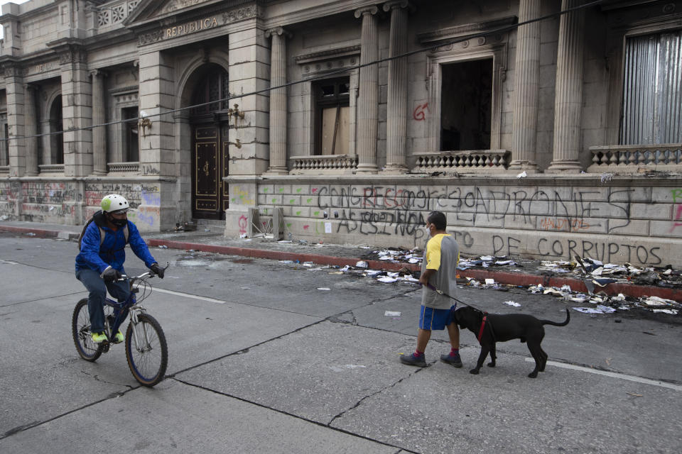 People walk past an area of the Congress building damaged during protests in Guatemala City, Sunday, Nov. 22, 2020. Protesters broke into the building and set it partially on fire amid growing demonstrations against President Alejandro Giammattei and the legislature for approving a controversial budget that cut educational and health spending. (AP Photo/Moises Castillo)