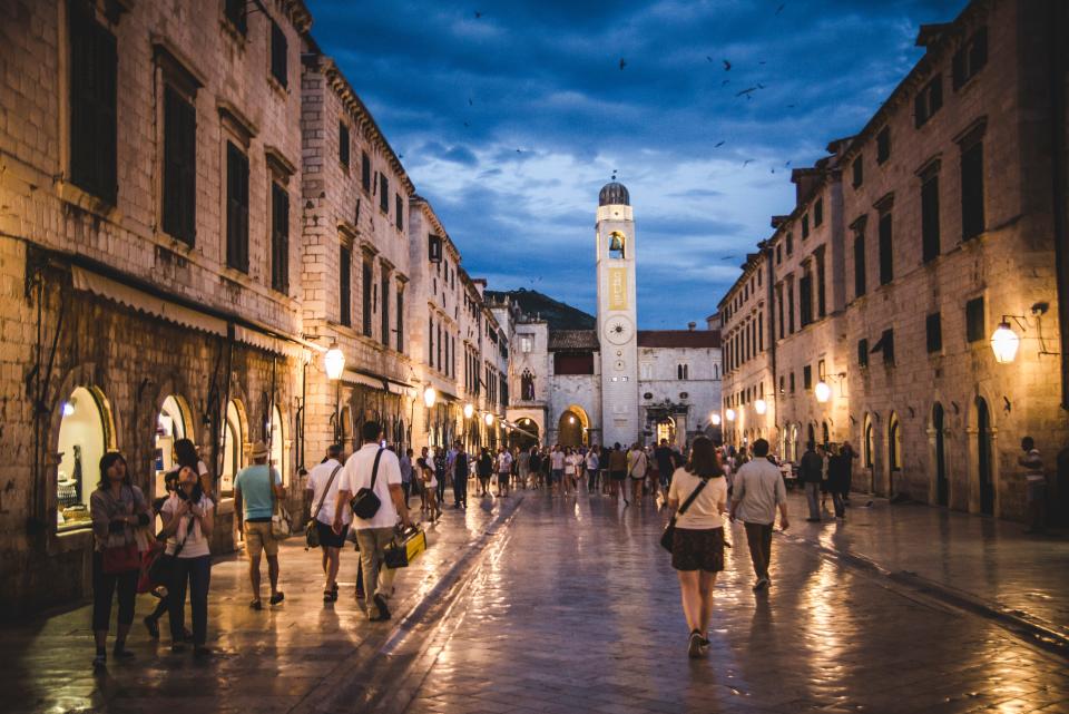 With the Adriatic Sea surrounding the city and breathtaking limestone mountains in the background, Old Town Dubrovnik is already a stunning site. Red roofs topping stone structures dot the coastal community, which was designated a <a href="https://www.britannica.com/place/Dubrovnik" rel="nofollow noopener" target="_blank" data-ylk="slk:UNESCO World Heritage Site;elm:context_link;itc:0;sec:content-canvas" class="link ">UNESCO World Heritage Site</a> in 1979. Stradun, or Placa, the main street in Old Town Dubrovnik, is not only a convenient way to see different parts of the city, but also beautiful in its own right. Running from Pile Gate—the western entrance to the historic area—to the port, the street is completely pedestrianized and full of shops, restaurants, and cafés. Stradun used to be a channel separating the island that the old town is built on from the mainland, but it was filled later to serve as the main street.