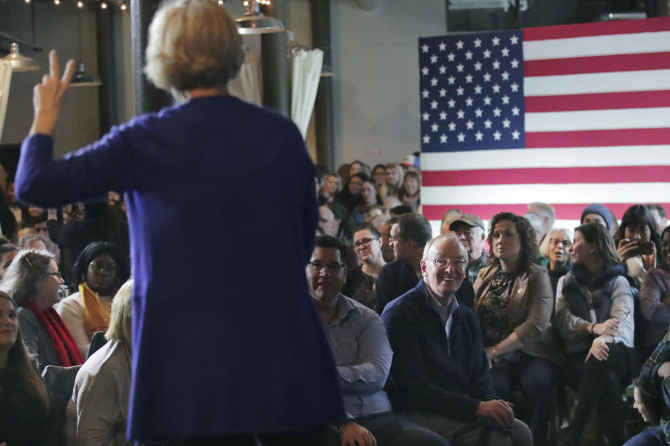 FILE - In this Jan. 10, 2020, file photo, Bruce Mann, husband of Democratic presidential candidate Sen. Elizabeth Warren, D-Mass., right, smiles as he listens to his wife during a campaign stop in Dover, N.H. (AP Photo/Charles Krupa, File)