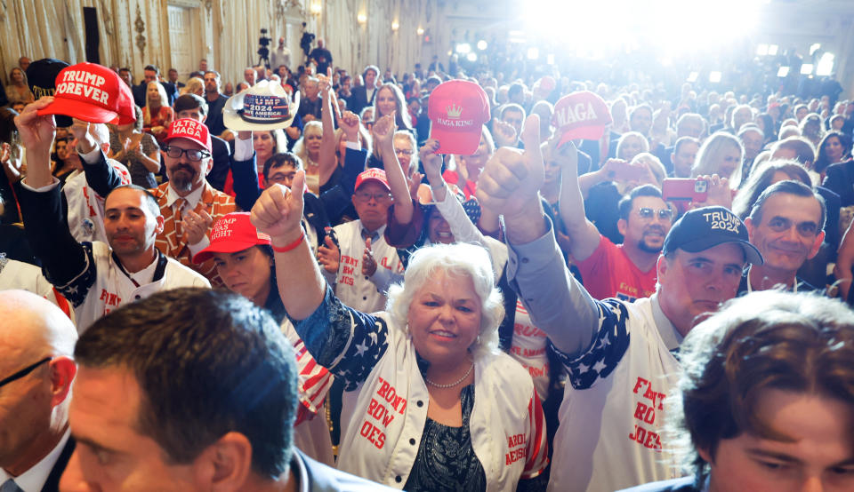 Supporters of former U.S. President Donald Trump wearing white jackets saying Front Row Joes in red letters hold up hats bearing slogans like MAGA King and Trump Forever.  