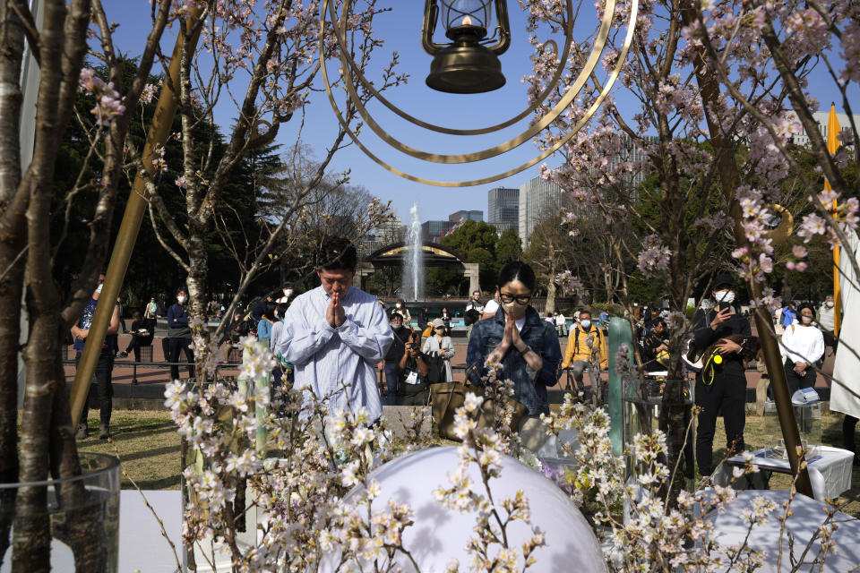 A man and a woman pray after laying flowers in front of a memorial set up to mark the 12th anniversary of the massive earthquake, tsunami and nuclear disaster, at Hibiya Park in Tokyo, Saturday, March 11, 2023. (AP Photo/Hiro Komae)