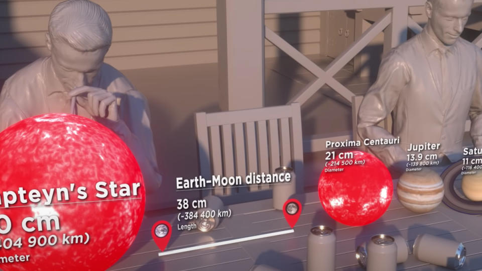 An animation of human-scale planets and stars in front of two people sitting behind a table.