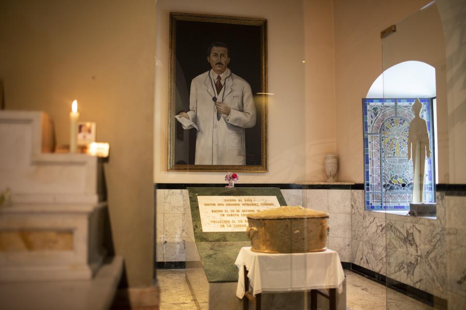 The remains of Venezuelan Dr. Jose Gregorio Hernandez popularly known as the "doctor of the poor", sit in an urn backdropped by his portrait, inside the Nuestra Senora de la Candelaria Catholic church, in Caracas, Venezuela, Friday, April 23, 2021. Hernandez is set to be beatified by the Catholic church, a step towards sainthood, on April 30th in the Venezuelan capital. (AP Photo/Ariana Cubillos)