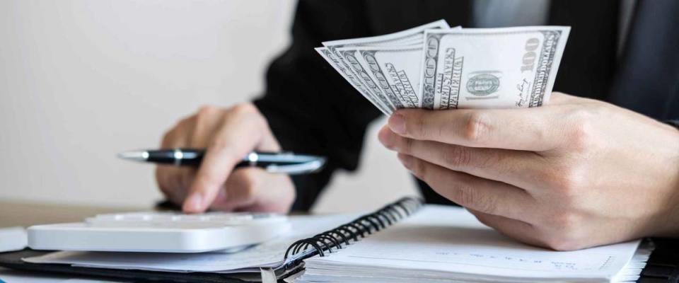 Close up of a man's hands holding a pile of cash and calculating something with his other hand.