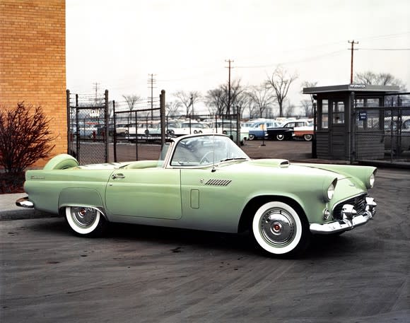 A green 1956 Ford Thunderbird, a low-slung two-seat convertible, is shown parked outside a building in 1956.