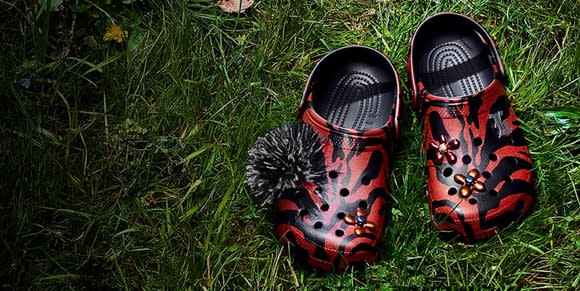 Red and black Crocs with special designs and inserts, sitting on a green grass lawn.