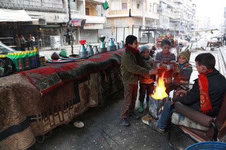 Children warm themselves next to an open fire beside fuel barrels, engine oil and accessories displayed for sale in Aleppo January 13, 2015. REUTERS/Nour Kelze