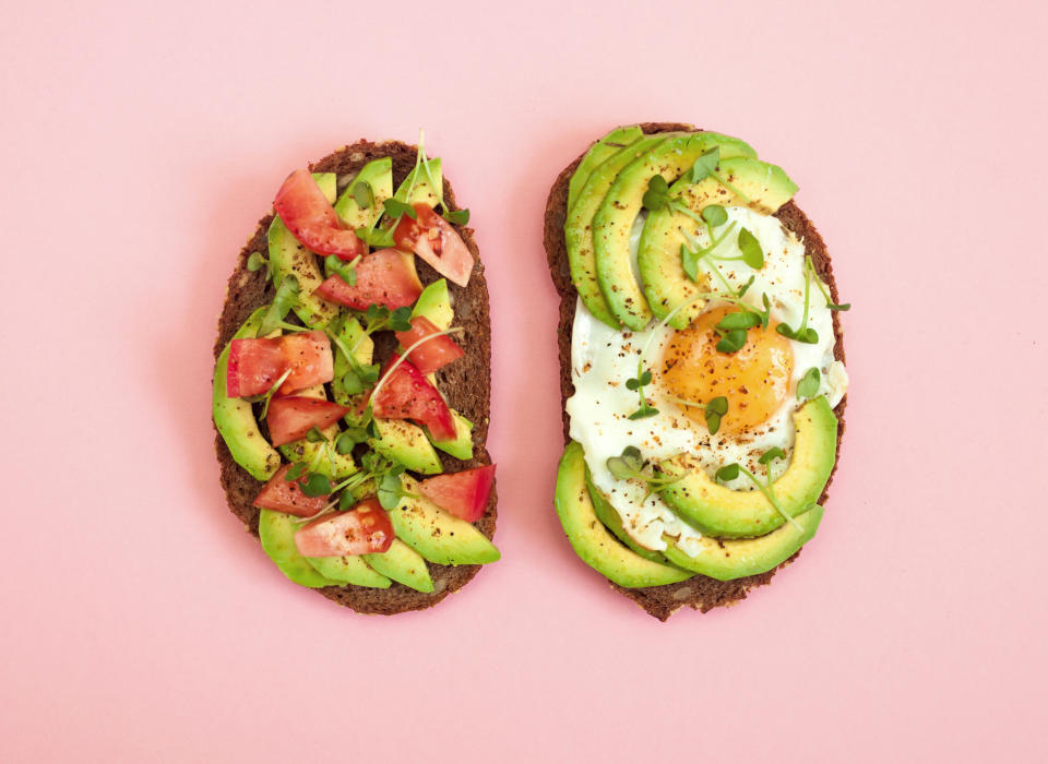 Toasts of dark bread with avocado slices, red tomatoes, fried egg and microgreen. Top view with pink background.