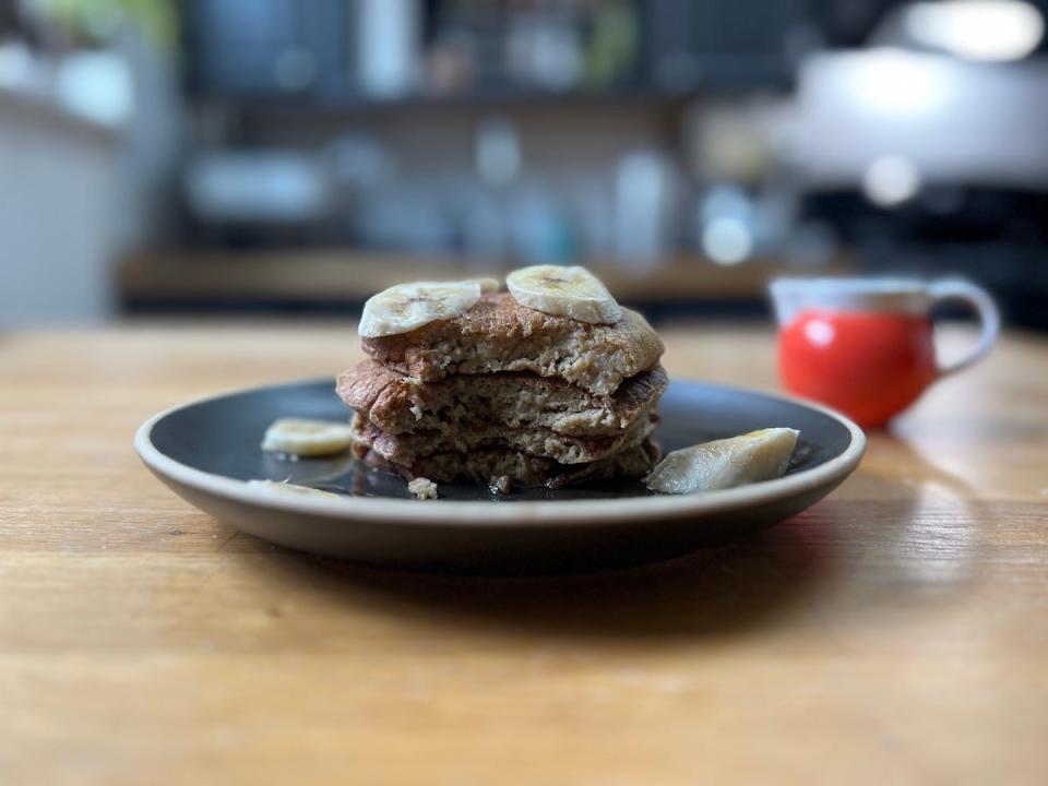 A plate of banana pancakes topped with chopped banana and maple syrup, that have been partially eaten.