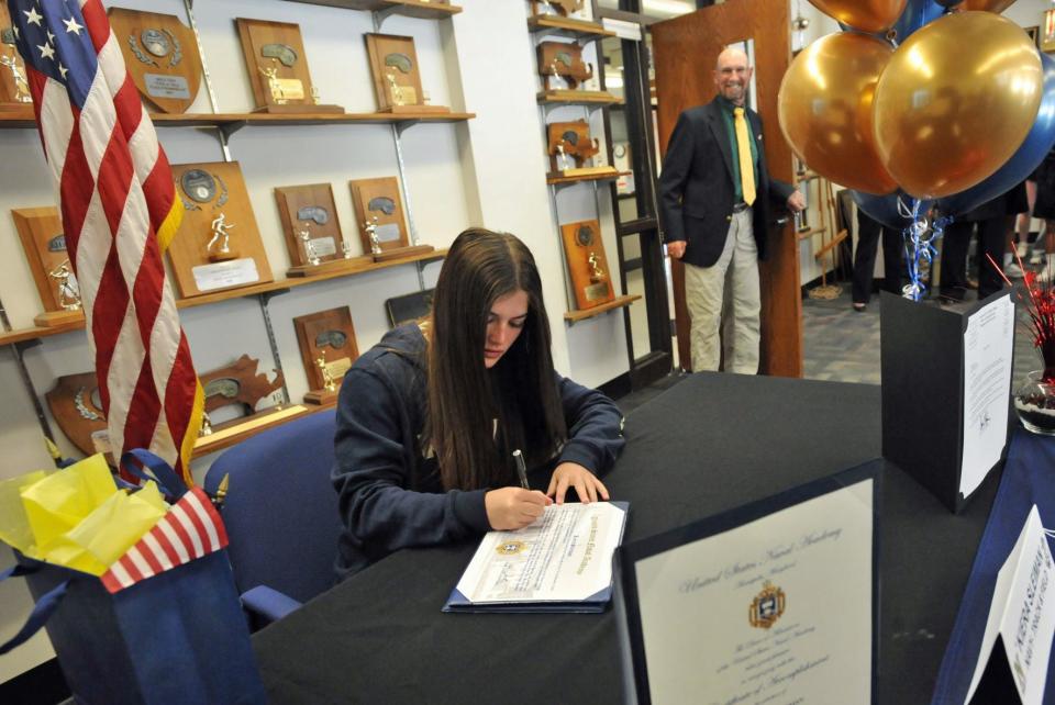 North Quincy High School senior and student-athlete  Kiera Sleiman signs her acceptance certificate to the United States Naval Academy as Quincy/North Quincy track & field coach Geoff Hennessy, right, looks on, during a ceremony at North Quincy High School on Friday, April 29, 2022.