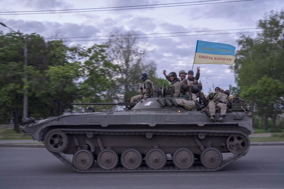 Ukrainian servicemen wave a flag with writing reading in Ukrainian "Glory to Ukraine", top, and "Death to the enemies" as they ride atop an armored vehicle in the Kharkiv region, eastern Ukraine, Monday, May 16, 2022.