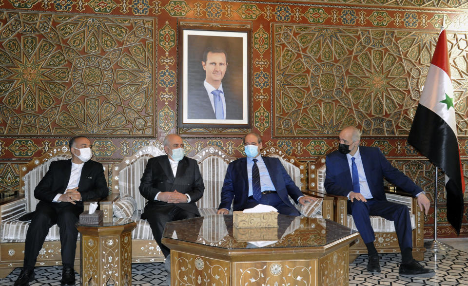 In this photo released by the Syrian official news agency SANA, Syria's Foreign Minister Faisal Mekdad, second right, receives his Iranian counterpart Mohammad Javad Zarif, second left, in Damascus, Syria, Wednesday, May 12, 2021. Zarif said his country is ready for closer ties with its regional rival Saudi Arabia, saying Wednesday he hoped recent talks would lead to greater stability in the region. A picture of Syrian President Bashar Assad hangs on the wall. (SANA via AP)