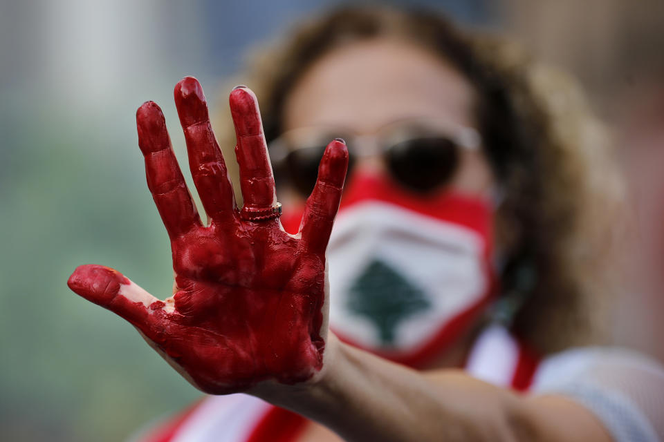 A Lebanese activist raises her hand painted red to represent blood, during a protest o demand answers and justice for the blast victims, near a house belonging to the Parliament speaker, in Beirut, Lebanon, Oct. 20, 2020. The blast was one of the largest non-nuclear explosions in history and six months later, political and confessional rivalries have undermined the probe into the Beirut port explosion and brought it to a virtual halt, mirroring the same rivalries that have thwarted past attempts to investigate political crimes throughout Lebanon's history. (AP Photo/Hussein Malla)