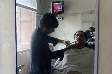 A man receives close shave as a television screen displays the coverage of Pakistan's Supreme Court's decision of disqualifying Pakistan's Prime Minister Nawaz Sharif, at a barber shop in Karachi, Pakistan July 28, 2017. REUTERS/Akhtar Soomro