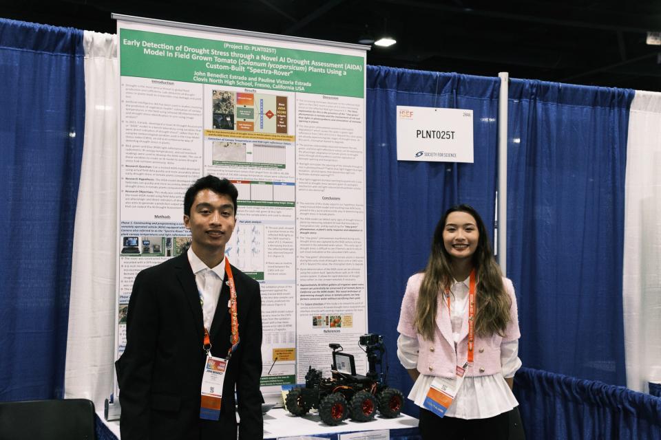 two teens in business clothes stand in front of a science fair project presentation board