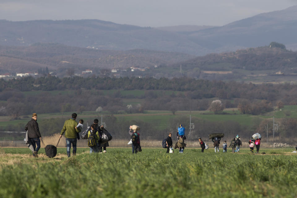 Refugee families walk through fields under mountains towards the Greek-Macedonian border.