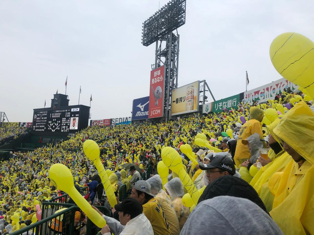 Fans holding up yellow balloons at a Hanshin Tigers baseball game in Japan.