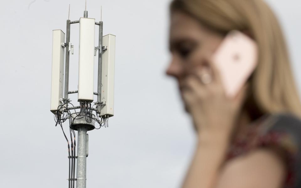 A pedestrian uses a mobile phone in view of antennas on a mobile telephone telecommunication mast - Jason Alden/Bloomberg