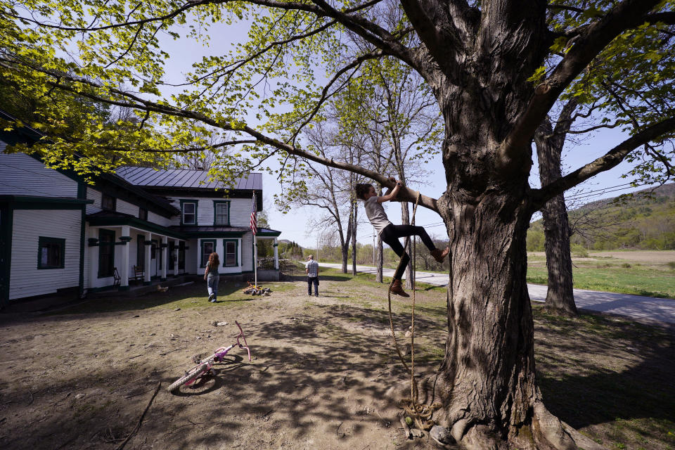 Soraya Holden climbs a tree with her parents in the background, Thursday, May 12, 2022, in Proctor, Vt. After fleeing one of the most destructive fires in California, the Holden family wanted to find a place that had not been so severely affected by climate change and chose Vermont. (AP Photo/Charles Krupa)