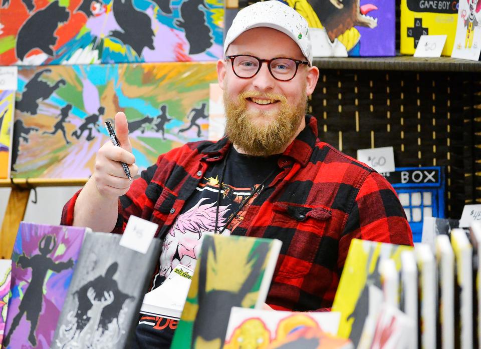 Surrounded by examples of his work, artist Zac Hnatyszyn, greets fans at Comicon Erie inside the Bayfront Convention Center in Erie in 2022.