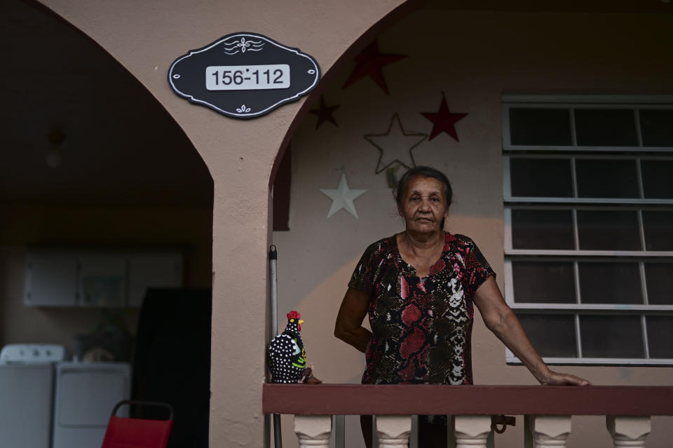 Candida Diaz poses for a photo by her homes' address number, which was registered for the first time by the iCasaPR, a nonprofit group that aims to standardize addresses on the island, in Caguas, Puerto Rico, Wednesday, Sept. 30, 2020. Puerto Rico’s municipalities and government agencies still use separate databases that use different names for the same streets or list the same addresses in varying ways. (AP Photo/Carlos Giusti)