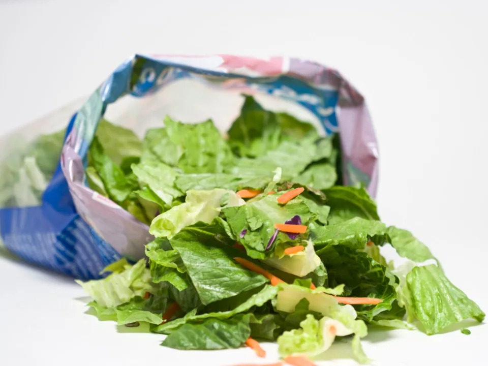 An opened bag of leafy greens and carrot salad