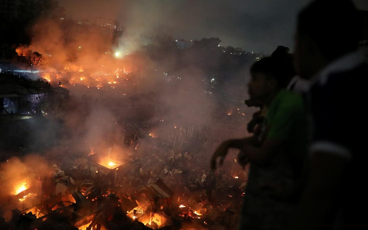 People gather at a rooftop to watch the fire that broke out at a slum in Dhaka - REUTERS