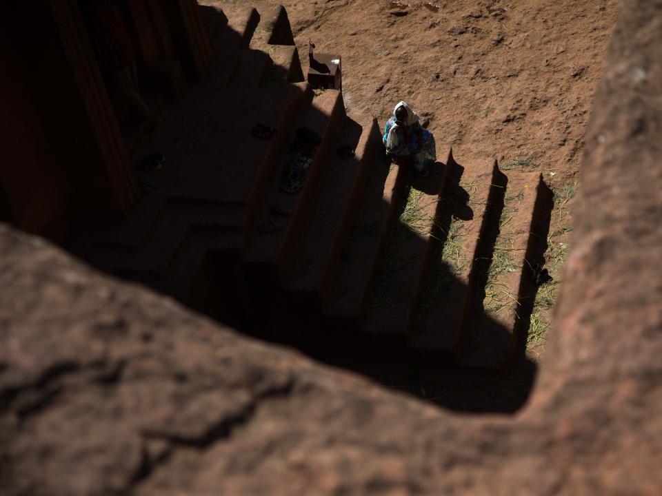 A shadow over a set of stone steps with a single person sitting on the side of them.