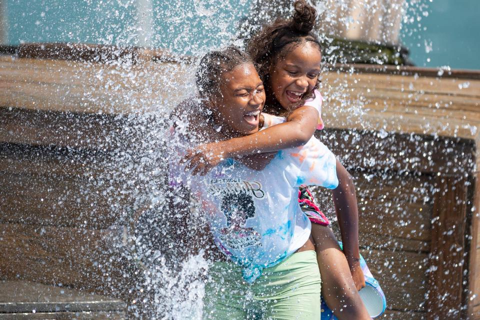 Navaeh Johnson, 14, carries cousin Kaniyah Hamilton, 8, on her back as they play at the splash pad in Mt. Elliott Park by the Detroit Riverfront on Wednesday, Aug. 3, 2022.