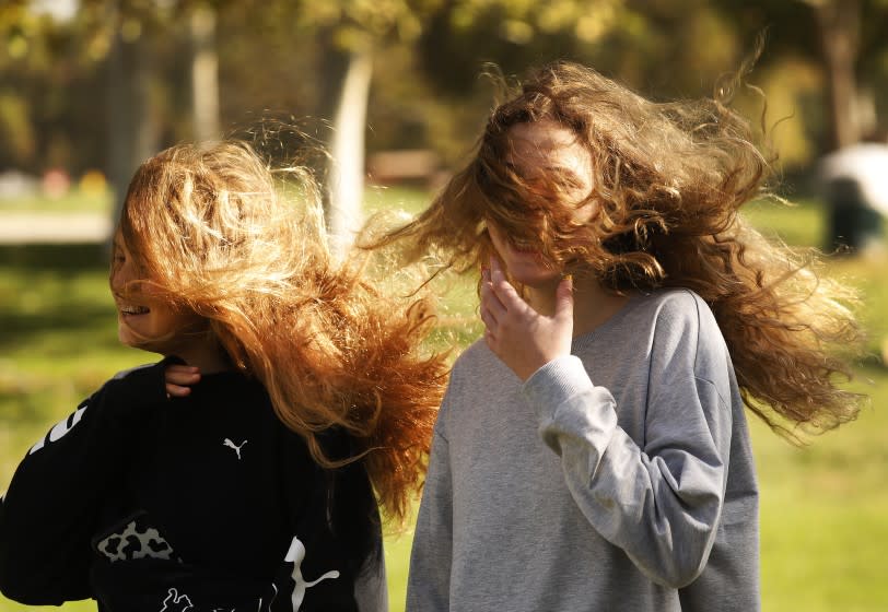 ENCINO, CA - OCTOBER 26: Hair out of control for best friends Angelina Skovlova, 13, left, and Mila Rubinstein, 15, as they brave the wind at Lake Balboa Beilenson Park in Encino Monday morning as the season's strongest Santa Ana winds are buffeting the Southland and combining with low humidity and dry vegetation to create what the National Weather Service calls the most dangerous fire weather conditions since October 2019. Lake Balboa Park on Monday, Oct. 26, 2020 in Encino, CA. (Al Seib / Los Angeles Times