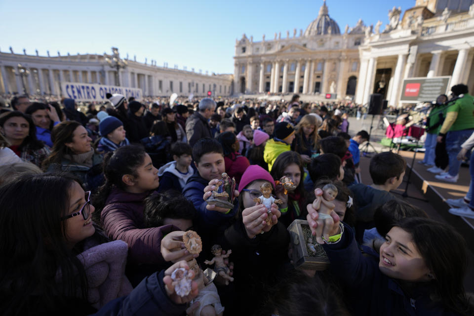 Children hold up statues of baby Jesus as they wait for Pope Francis' Angelus noon prayer he celebrates from the window of his studio overlooking St.Peter's Square, at the Vatican, Sunday, Dec. 17, 2023. (AP Photo/Alessandra Tarantino)