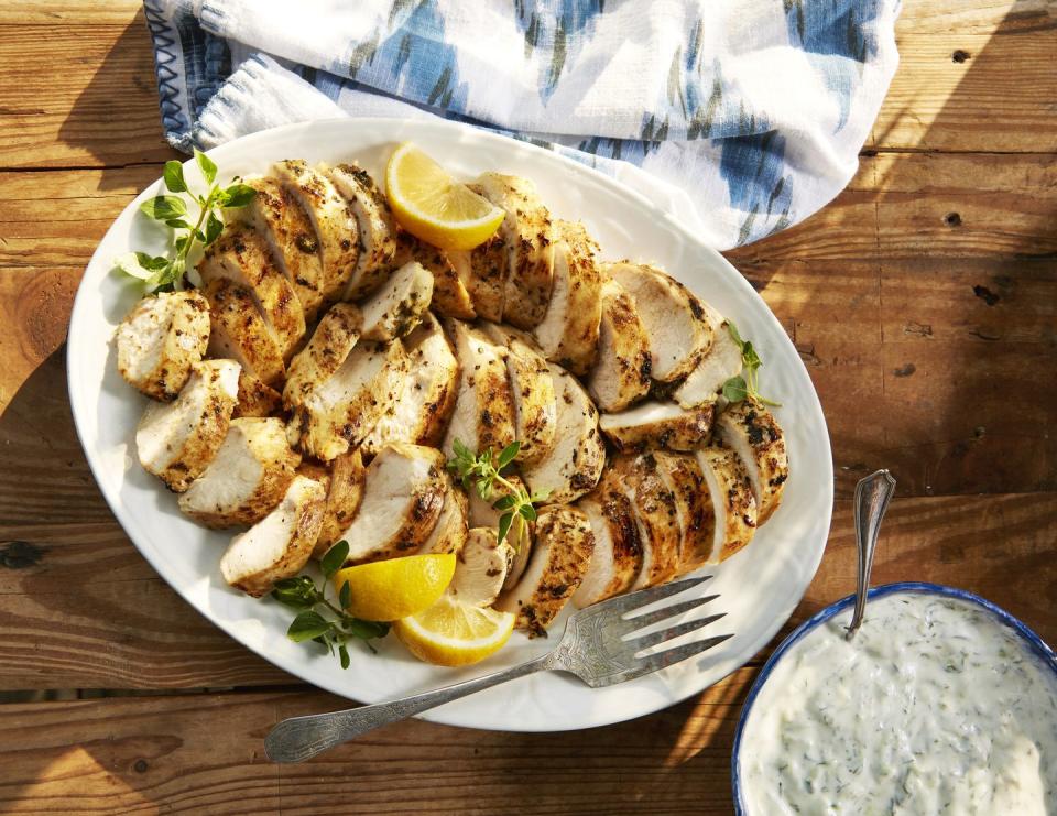 greek chicken on a plate with lemon wedges and tzatziki sauce