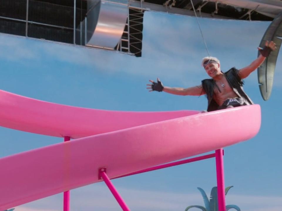 Ryan Gosling in leather vest sliding down a pink slide in Barbie