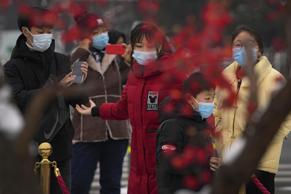 Visitors wearing face masks to help protect from the coronavirus gather to take souvenir photo with a decoration for the Lunar New Year at Qianmen Street, a popular tourist spot in Beijing, Sunday, Jan. 23, 2022. Chinese authorities have called on the public to stay where they are during the Lunar New Year instead of traveling to their hometowns for the year's most important family holiday. (AP Photo/Andy Wong)