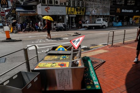 People go about their day past fallen street signs, recycle bins and barricade after yesterday's protests in Tsuen Wan, Hong Kong