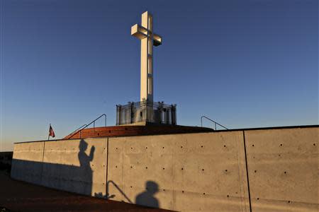 People are silhouetted against a wall as they photograph the massive cross sitting atop the Mt. Soledad War Memorial in La Jolla, California on December 12, 2013. REUTERS/Sandy Huffaker