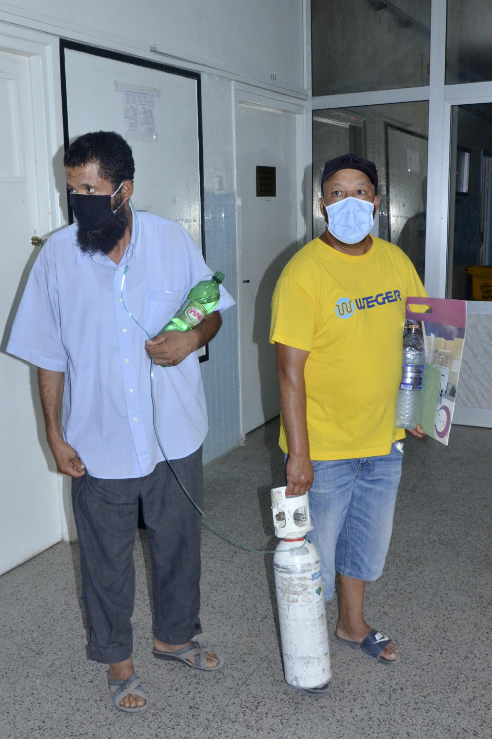 FILE - In this June 28, 2021, file photo, a man with the COVID-19 virus, left, is assisted with an oxygen tank at the Iben El Jazzar hospital, in Kairouan, Tunisia. As Tunisia faces a surge of COVID-19 cases, demand for life-saving oxygen has grown higher than the supply, leaving patients desperate and family members angry at the government as they say they are forced to find oxygen on their own. (AP Photo/Aimen Othmani, File)