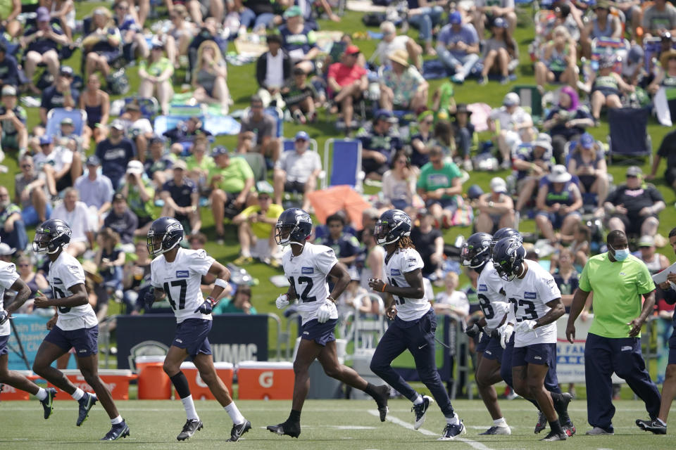 FILE - Seattle Seahawks defensive players run on the field as fans watch NFL football practice in Renton, Wash., in this Wednesday, July 28, 2021, file photo. It's not exactly everyone into the pool, or gathering around the bonfire. The NFL's “Back Together Saturday” at training camps is all about football. Well, also about having fans return to watch, with all 32 teams conducting open practices on Saturday, July 31, as part of a unified effort by the league. (AP Photo/Ted S. Warren, File)