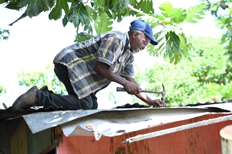 A man hammers nails on a tin roof.